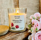 A coconut wax candle labeled 'Bohemian Rose' with a wooden wick, decorated with floral illustrations and burning on a wooden surface, alongside pink roses.
